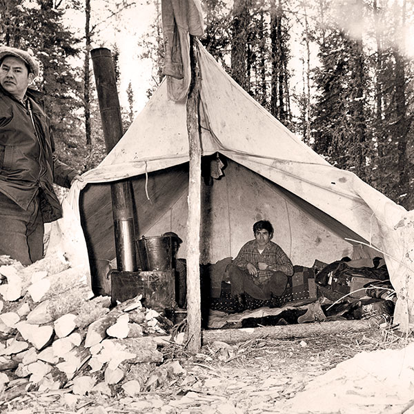 Indigenous worker siting in his tent beside a wood stove.