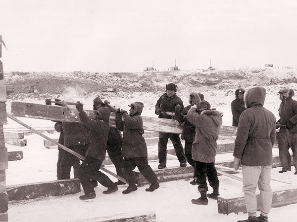 A group of men lifting a wooden beam.